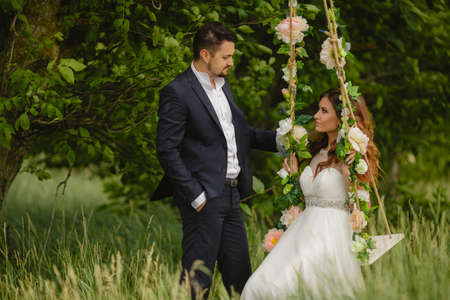 Beautiful young wedding pair in park, the bride in a white wedding dress on fluctuation and her groom.の写真素材
