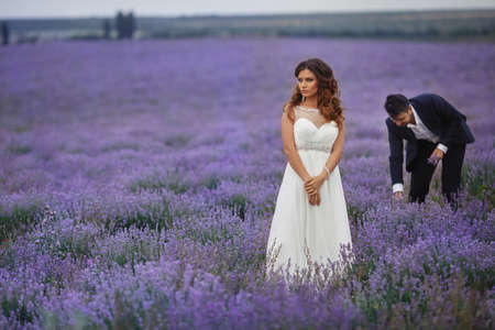 A young couple in love bride and groom, wedding day in summer. Enjoy a moment of happiness and love in a lavender field. Bride in a luxurious wedding dress on a background bright blue sky .の写真素材