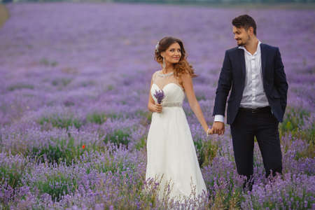 A young couple in love bride and groom, wedding day in summer. Enjoy a moment of happiness and love in a lavender field. Bride in a luxurious wedding dress on a background bright blue sky .の写真素材