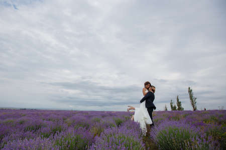 A young couple in love bride and groom, wedding day in summer. Enjoy a moment of happiness and love in a lavender field. Bride in a luxurious wedding dress on a background bright blue sky .の写真素材