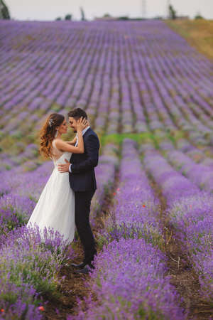 A young couple in love bride and groom, wedding day in summer. Enjoy a moment of happiness and love in a lavender field. Bride in a luxurious wedding dress on a background bright blue sky .の写真素材