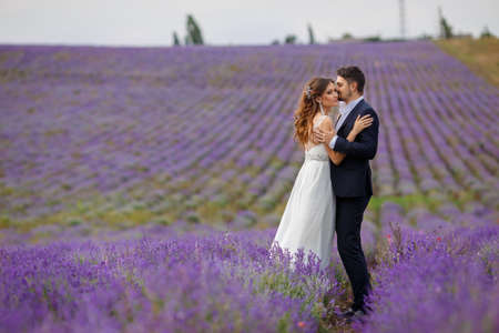 A young couple in love bride and groom, wedding day in summer. Enjoy a moment of happiness and love in a lavender field. Bride in a luxurious wedding dress on a background bright blue sky .の写真素材