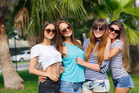 Beautiful girls are photographed on a tropical resort on a background of green nature.Four young beautiful girls - brunette, long straight hair, in shorts and T-shirts, sun glasses, with a beautiful smile, photographed on a smartphone on a background of tの写真素材
