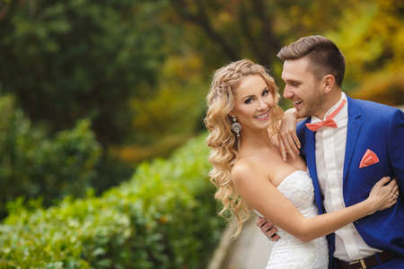 Bride and groom at wedding Day walking Outdoors on spring nature. Bridal couple, Happy Newlywed woman and man embracing in green park. Loving wedding couple outdoor. Bride and groom