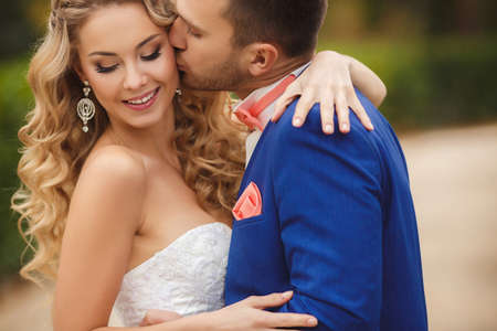Bride and Groom at wedding Day walking Outdoors on summer green nature. Bridal couple, Happy Newlywed woman and man embracing and kissing in green park. Loving wedding couple outdoor. Bride and groomの写真素材
