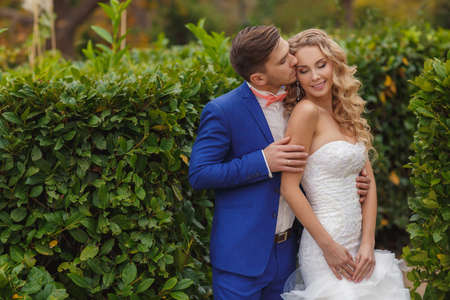 Bride and Groom at wedding Day walking Outdoors on summer green nature. Bridal couple, Happy Newlywed woman and man embracing and kissing in green park. Loving wedding couple outdoor. Bride and groomの写真素材