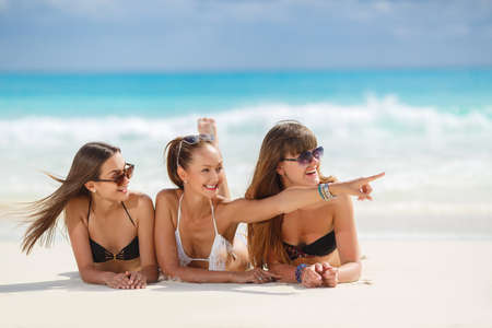 Three slim young girls in bikinis on the beach. summer holidays and vacation - girls in bikinis sunbathing on the beach.の写真素材