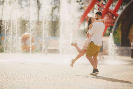 A young couple, a man of Caucasian appearance, with short hair and a beautiful beard, white shirt and bow tie and the girl-long-haired brunette in a light pink dress with bare shoulders walking and hugging in the Park in the summer.の写真素材