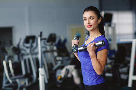Strong woman weightlifting at the gym. Woman working out with dumbbells at a gym. Dumbbell bicep...