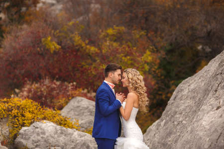 The bride and groom - the photograph in the Park.groom - a young dark-haired man in a blue suit and pink wedding tie - butterfly kisses on the cheek bride, blue-eyed - curly blond with long hair in white wedding dress in summer park.の写真素材