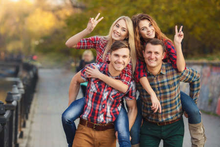 four friends, two women and two men relax and have fun in autumn park, girl, long-haired blonde and brunette in a blue denim dress, the other in a red plaid shirt, men-both brunettes in a blue denim shirt, the other in a T-shirt.の写真素材