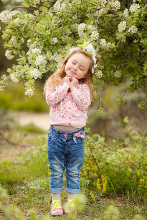 Cute little girl on the meadow in spring day. portrait of little girl outdoors in blooming parkの写真素材