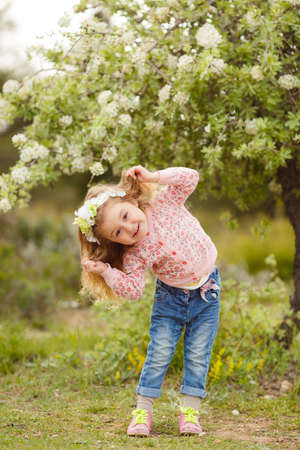 Cute little girl on the meadow in spring day. portrait of little girl outdoors in blooming parkの写真素材