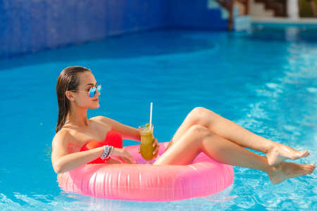 Young pretty fashion woman body posing in summer in pool with clear water lying inner tube and...