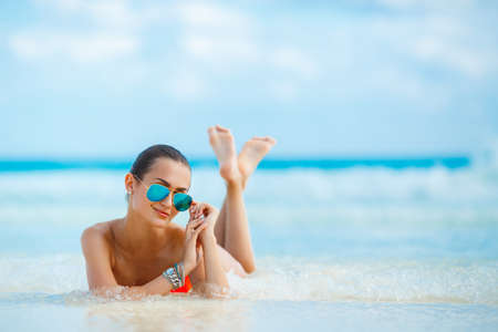 Attractive and sexy girl on the beach. Young female enjoying sunny day on tropical beach. Beautiful girl sunbathing under summer sun lying in sand on beach with blue waterの写真素材