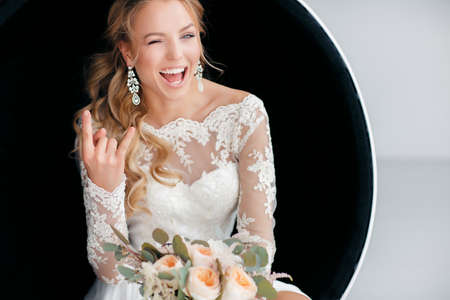 Young attractive bride with a wedding bouquet.Wedding portrait of happy blueeyed bride with long curly hairbeautiful smilemakeupwhite wedding dressearrings in your earsholding a large bouquet of beautiful natural roses delicate cream colorの写真素材