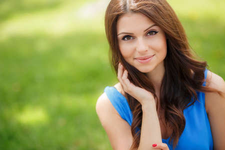 Portrait close up of young beautiful woman, on green background summer nature.A beautiful young woman, a brunette with big brown eyes and long hair, dressed in a light blue blouse, posing in the summer on a background of green in the city Parkの写真素材