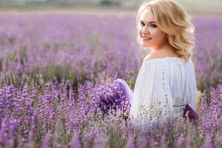 Beautiful Bride in lavender field. Newlywed woman in lavender flowers.Young woman in wedding dress outdoors. Beautiful young woman in white dress posing in a lavender field with small wicker basketの写真素材