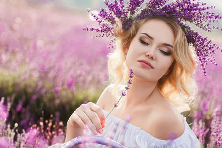 Beautiful Bride in lavender field. Newlywed woman in lavender flowers.Young woman in wedding dress outdoors. Beautiful young woman in white dress posing in a lavender field with small wicker basketの写真素材