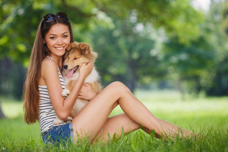 woman beautiful young happy with long dark hair in striped sweater holding collie dog. Young woman playing with Collie puppy outdoors in the park.の写真素材