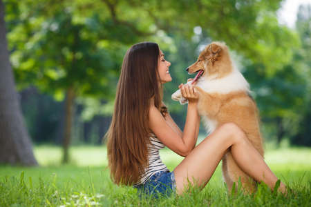 woman beautiful young happy with long dark hair in striped sweater holding collie dog. Young woman playing with Collie puppy outdoors in the park.の写真素材