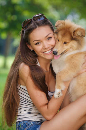 woman beautiful young happy with long dark hair in striped sweater holding collie dog. Young woman playing with Collie puppy outdoors in the park.の写真素材