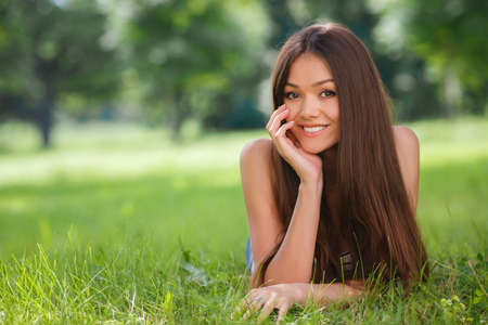 Beautiful smiling woman lying on a grass outdoor. She is absolutely happy.lifestyle, summer vacation, leisure and people concept - smiling young girl lying on grass in parkの写真素材