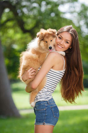 woman beautiful young happy with long dark hair in striped sweater holding collie dog. Young woman playing with Collie puppy outdoors in the park.の写真素材