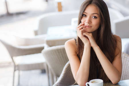 pretty young woman sitting in cafe with a cup of tea or coffee outdoor. Charming woman in a restaurant. Woman with coffeeの写真素材