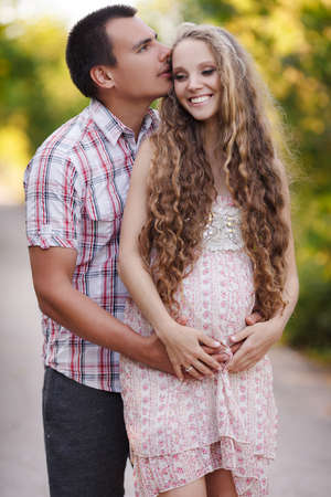 young happy family. man and a pregnant woman happy nature. Happy beautiful pregnant woman with his husband sitting on the lawn outside. Family together in the summer park. Woman is pregnantの写真素材