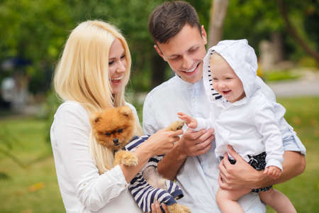 Happy young family, mother-blonde with a little red dog, dad, dark man with a young son, spend a day in a city park on the outdoors and having fun playing together on a background of green natureの写真素材