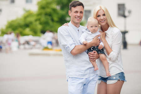 Happy young family, mother-blonde with a little red dog, dad, dark man with a young son, spend a day in a city park on the outdoors and having fun playing together on a background of green natureの写真素材