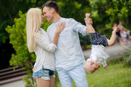 Happy young family, mother-blonde with a little red dog, dad, dark man with a young son, spend a day in a city park on the outdoors and having fun playing together on a background of green natureの写真素材