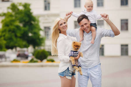 Happy young family, mother-blonde with a little red dog, dad, dark man with a young son, spend a day in a city park on the outdoors and having fun playing together on a background of green natureの写真素材