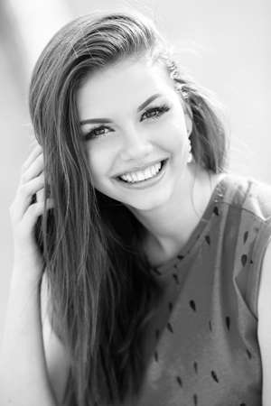 Summer portrait of beautiful red-haired woman with brown eyes and a sweet smile, dressed in a red blouse sleeveless outdoors on a warm summer day in the cityの写真素材