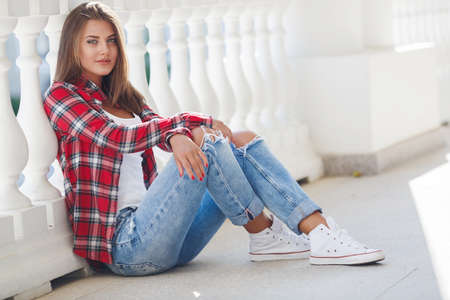 Portrait Of Young Smiling Beautiful Woman. fashionable casual woman sitting on the floor in city streetの写真素材