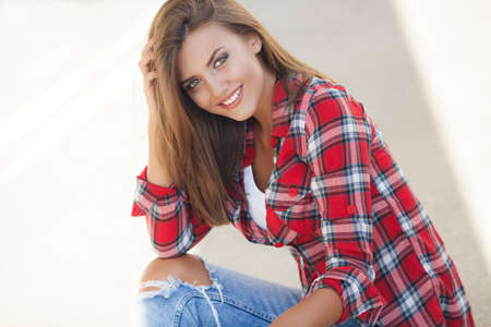 Portrait Of Young Smiling Beautiful Woman. fashionable casual woman sitting on the floor in city streetの写真素材