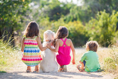 Three children with two labrador retrievers outdoor in summer park.Little girls and a boy playing with two labrador retrievers in the summer park. children and dogsの写真素材