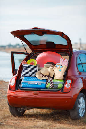 Suitcases and bags in trunk of car ready to go on vacation, the red car with an open trunk loaded to capacity with things to relax, on the beach near the sea, a trip into the countryside for a happy familyの写真素材