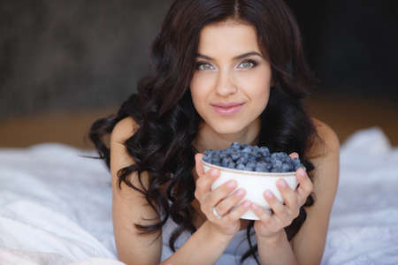 woman laying on the floor with bowl of berries blueberries at home. fresh morning. healthcare. Portrait of beautiful young woman eating a bowl of blueberries and smiling. Healthy food.の写真素材