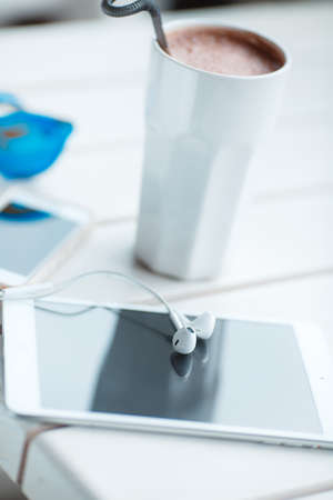 Digital tablet computer with cup of coffee on old wooden table in white cafe. Simple workspace or coffee break with web surfing. bue sunglassesの写真素材