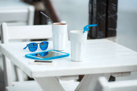 Digital tablet computer with cup of coffee on old wooden table in white cafe. Simple workspace or coffee break with web surfing. bue sunglassesの写真素材