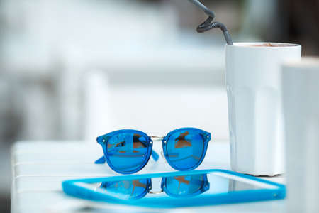 Digital tablet computer with cup of coffee on old wooden table in white cafe. Simple workspace or coffee break with web surfing. bue sunglassesの写真素材