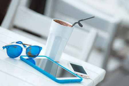 Digital tablet computer with cup of coffee on old wooden table in white cafe. Simple workspace or coffee break with web surfing. bue sunglassesの写真素材