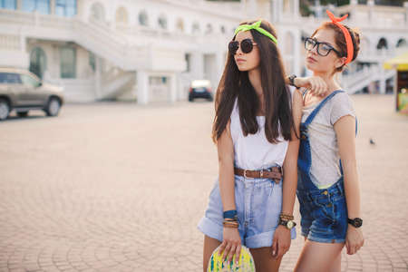 Two teen girl friends having fun together with skate board. Outdoors, urban lifestyle. Toned. Two beautiful and young girlfriends having fun with a skateboard.の写真素材