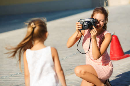 Mother making photos of her daughter child. Mother photograph child outdoor. Mother with camera. Child posing to the camera. Mother photographing her daughterの写真素材
