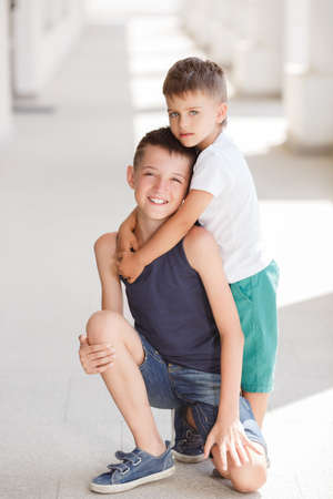 Two schoolboys, cute guys, older and younger brother, both dark-haired with short hair, in shirts and shorts, spend vacation time together, having fun and walking around the city together in the summer.の写真素材