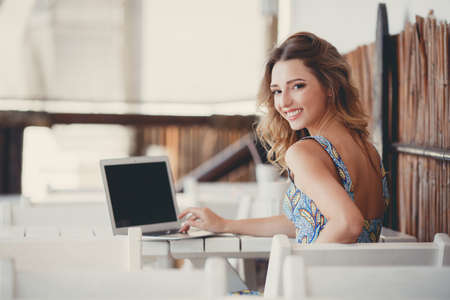 Beautiful woman using laptop at cafe. Young woman with coffee and laptop. Portrait of beautiful smiling woman sitting in a cafe with black laptop.の写真素材
