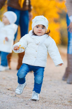 Little girl in yellow autumn park.Funny cute little girl in a white jacket, hat and white shoes, with big brown eyes, walking down the Avenue of beautiful, yellow, autumn Park Sunny day, walking with my mom and girlfriendの写真素材