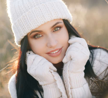 Portrait of a young, beautiful woman, brunette with long straight hair and gray-green eyes, beautiful smile and light makeup, dressed in a white sweater, white gloves and a white cap, autumn photo shoot models outdoors in fieldの写真素材